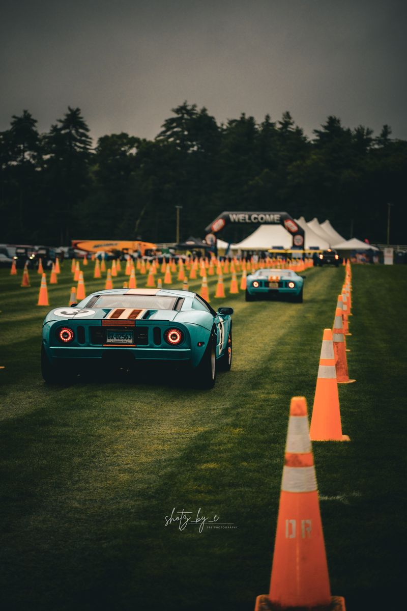 Two blue Ford GTs between orange cones at a car meet