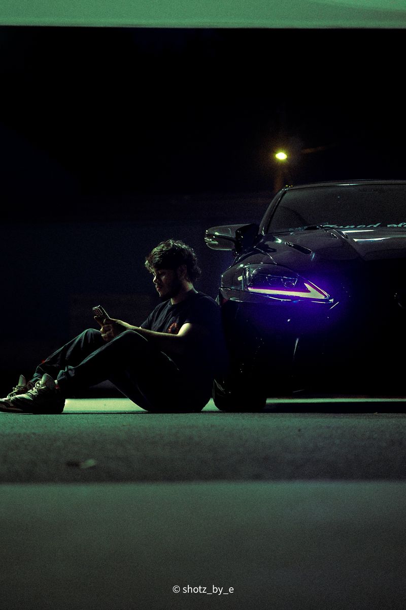 Man sitting beside a Lexus at night